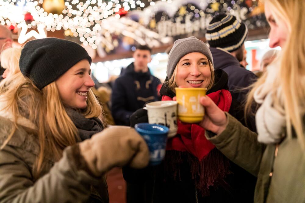 Freundinnen stoßen auf einem Weihnachtsmarkt mit Glühweintassen an